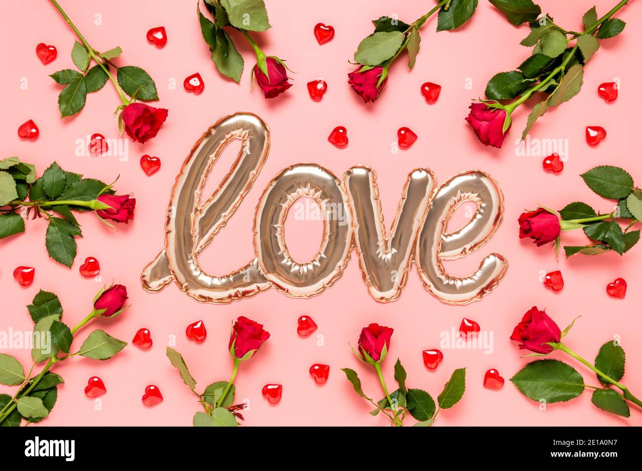Liebe Wort mit glänzend geformten goldenen Folienballon mit roten Rosen und Herzen auf rosa Hintergrund umgeben gemacht. Muttertag, Frauentag oder Valentinstag Stockfoto