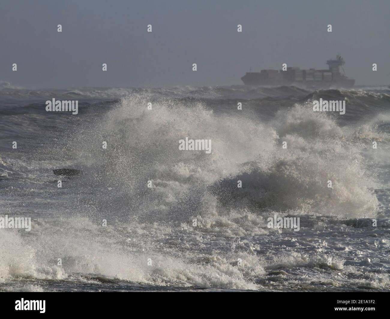 Sturm an der Küste mit brechenden Wellen, Spritzwasser, Spray und einem Schiff am Horizont (Fokus auf den Vordergrund). Stockfoto