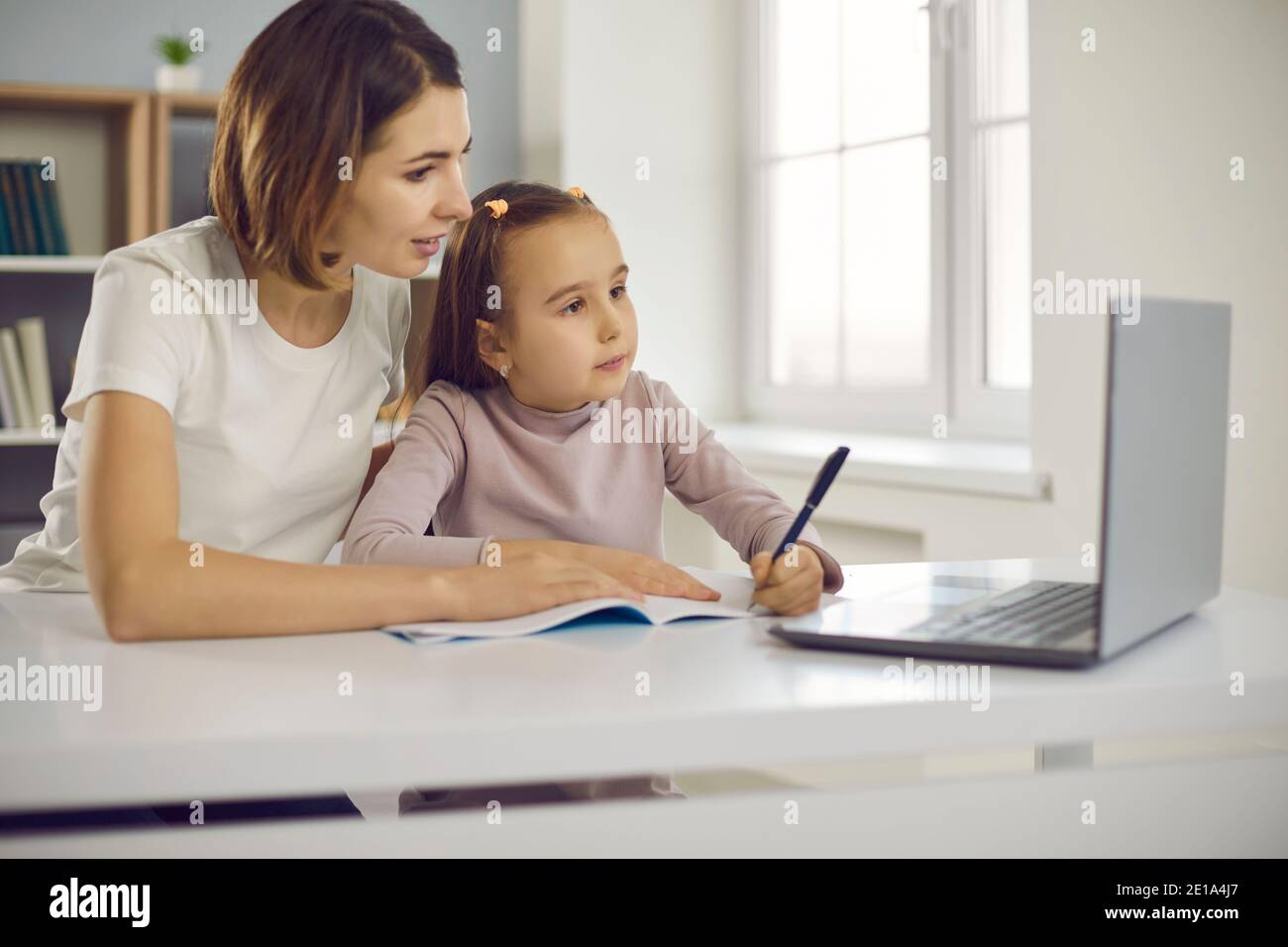 Kleine positive Mädchen und ihre Mutter zeichnen oder Alphabet lernen Und schreiben während des Online-Unterrichts Stockfoto
