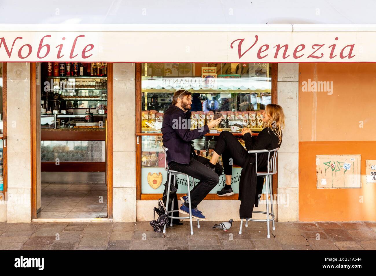 Ein glückliches Paar, das Kaffee trinkt und Gebäck vor einem Café in Venedig, Italien, isst. Stockfoto
