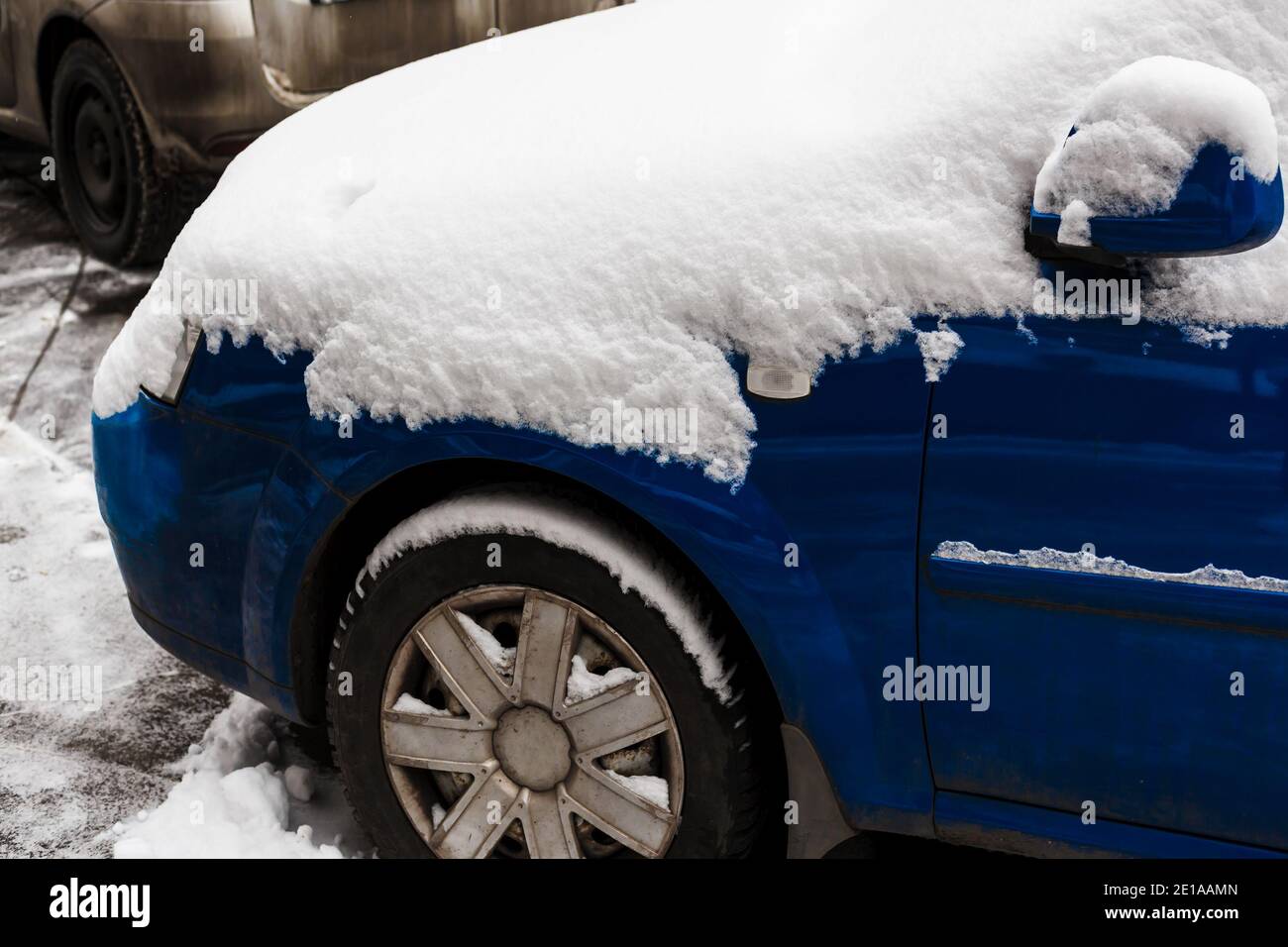 Blauer Autostoßfänger mit dicken Schneeschicht bedeckt. Kalter Zyklon. Transportschwierigkeiten bei Schneefall Stockfoto