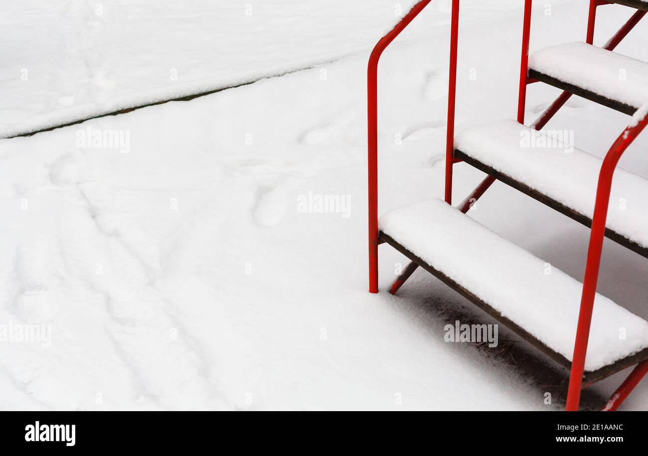 Frischer weißer Schnee auf einer Leitertreppe. Veranda mit rotem Geländer mit Schnee bedeckt Stockfoto