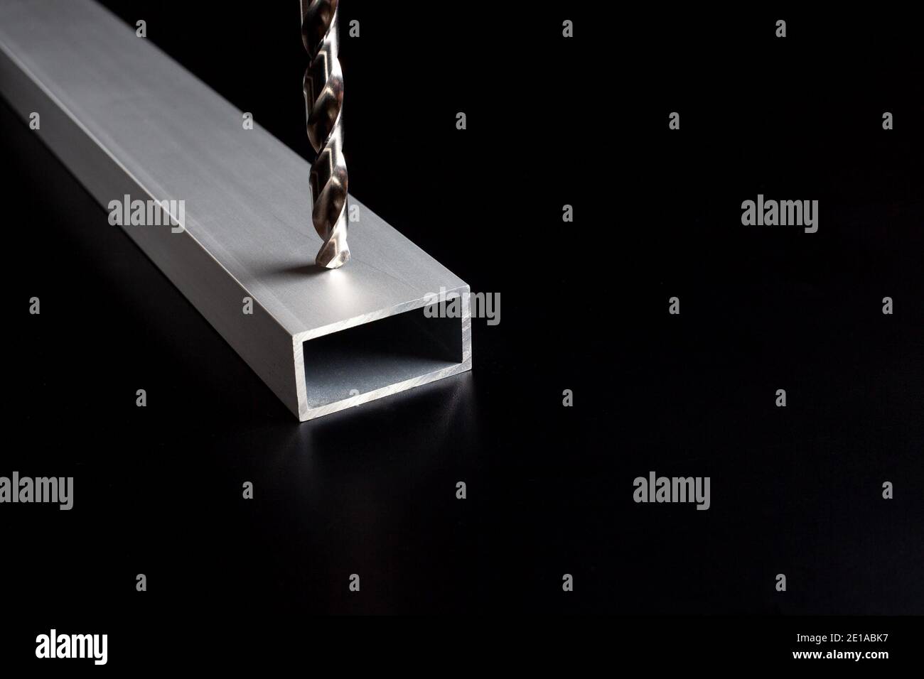 Bohren Sie ein Profilrohr aus Aluminium-Stahl auf dunklem Oberflächenhintergrund. Löcher in Metall machen Stockfoto