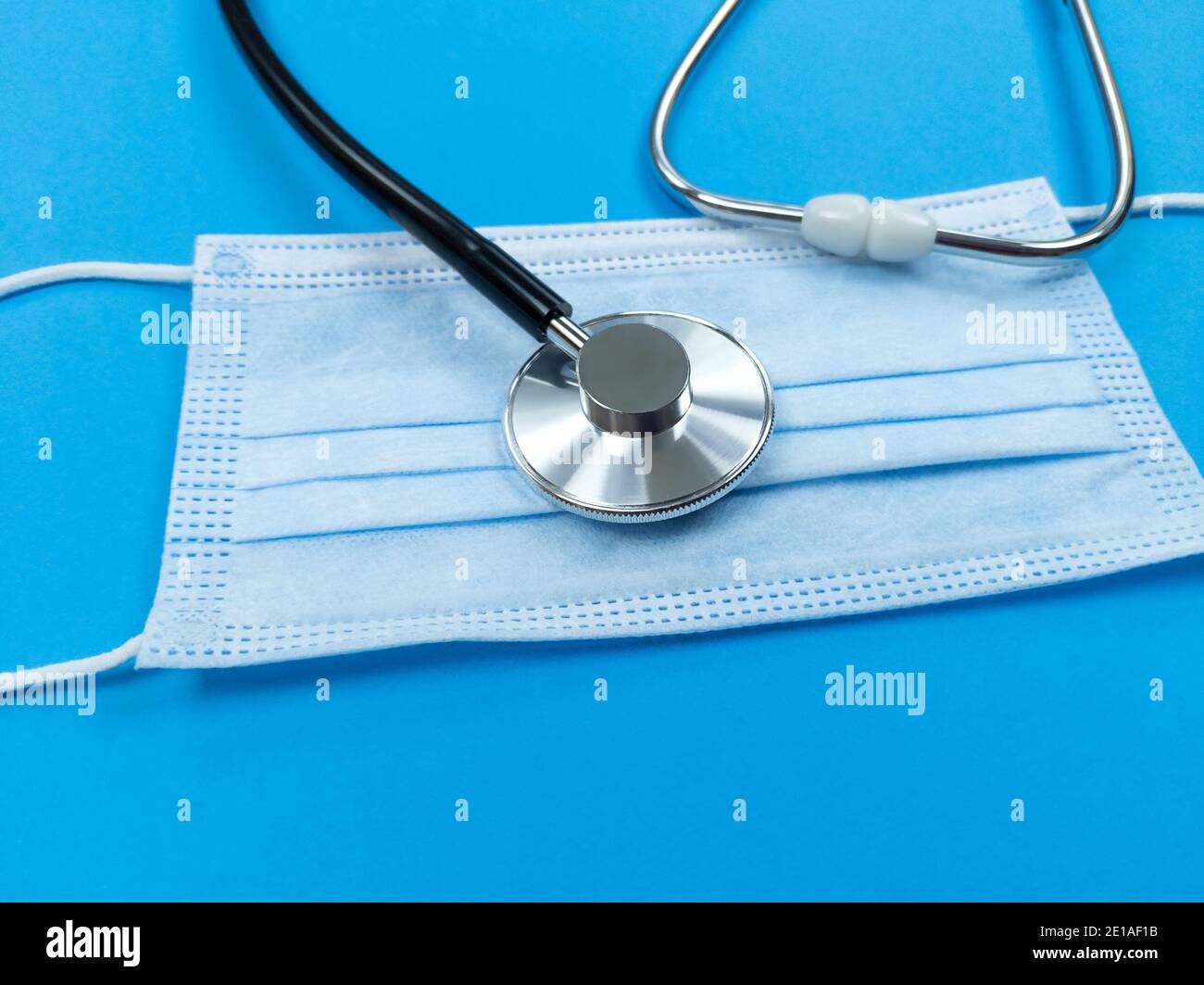 Schwarzes Stethoskop auf Einweg-Gesichtsmaske auf blauem Hintergrund. Medizinisches Konzept. Stockfoto