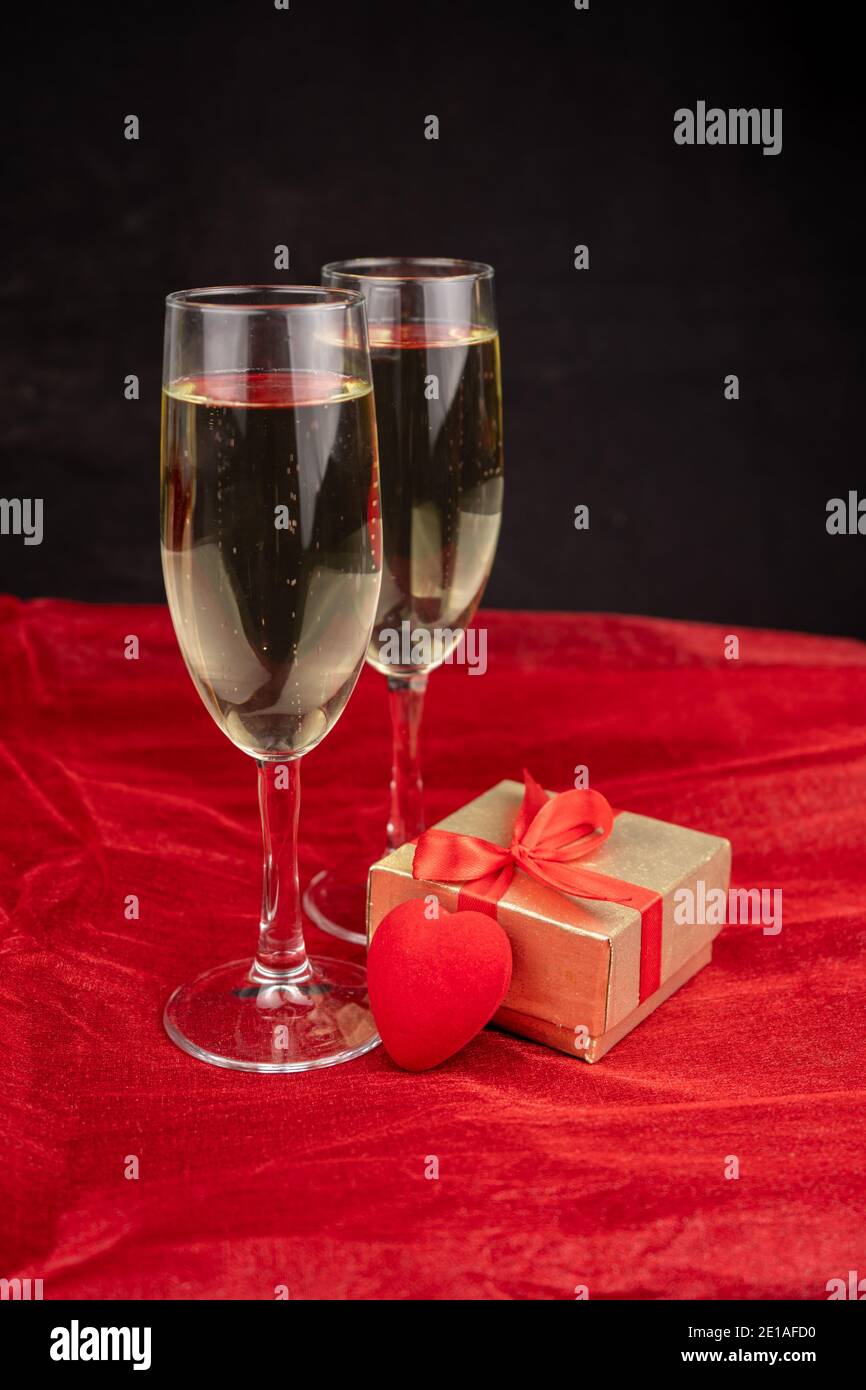 Zwei Gläser mit Champagner, goldener Geschenkbox und romantischem Dekor auf schwarzem und rotem Hintergrund Stockfoto