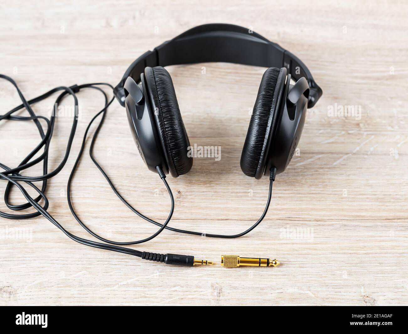 Schwarz verdrahtete Ohrhörer mit goldenem TRS-Adapter und -Buchse auf einem Schreibtisch. Vergoldete Stecker für hochwertige Audioqualität. Gadget für das Hören von Musik. Stockfoto