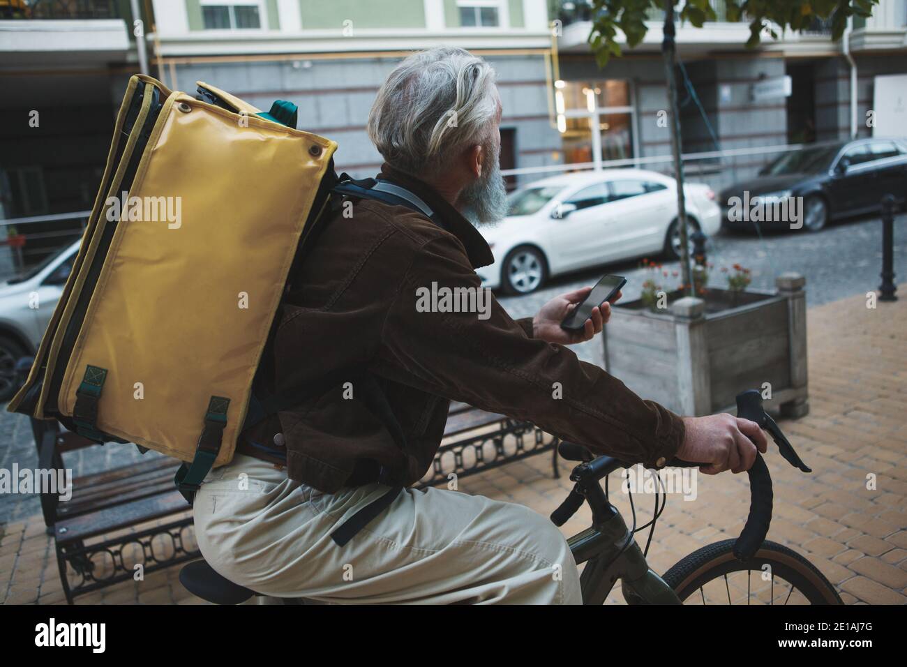 Rückansicht eines älteren Lieferers, der Fahrrad fährt und einen Rucksack trägt Stockfoto