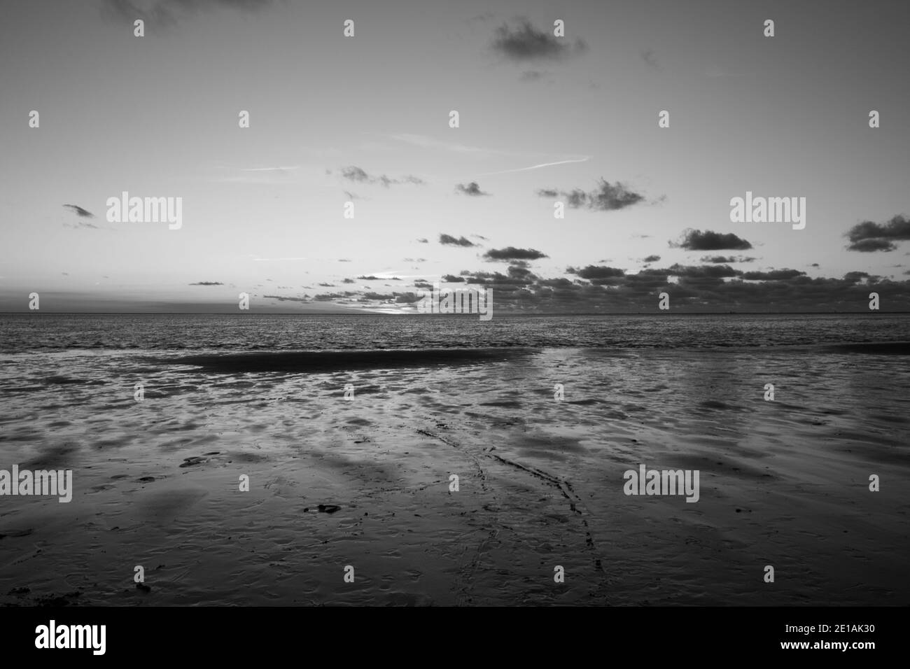 Schwarz und weiß Blick auf die untergehende Sonne, die auf dem Meer scheint und sich am Strand spiegelt, Wolken mit sonnenscheinenden Rändern. Querformat. Hochwertige Foto zeigt Konzept der Freiheit und Träume in monochrom Stockfoto