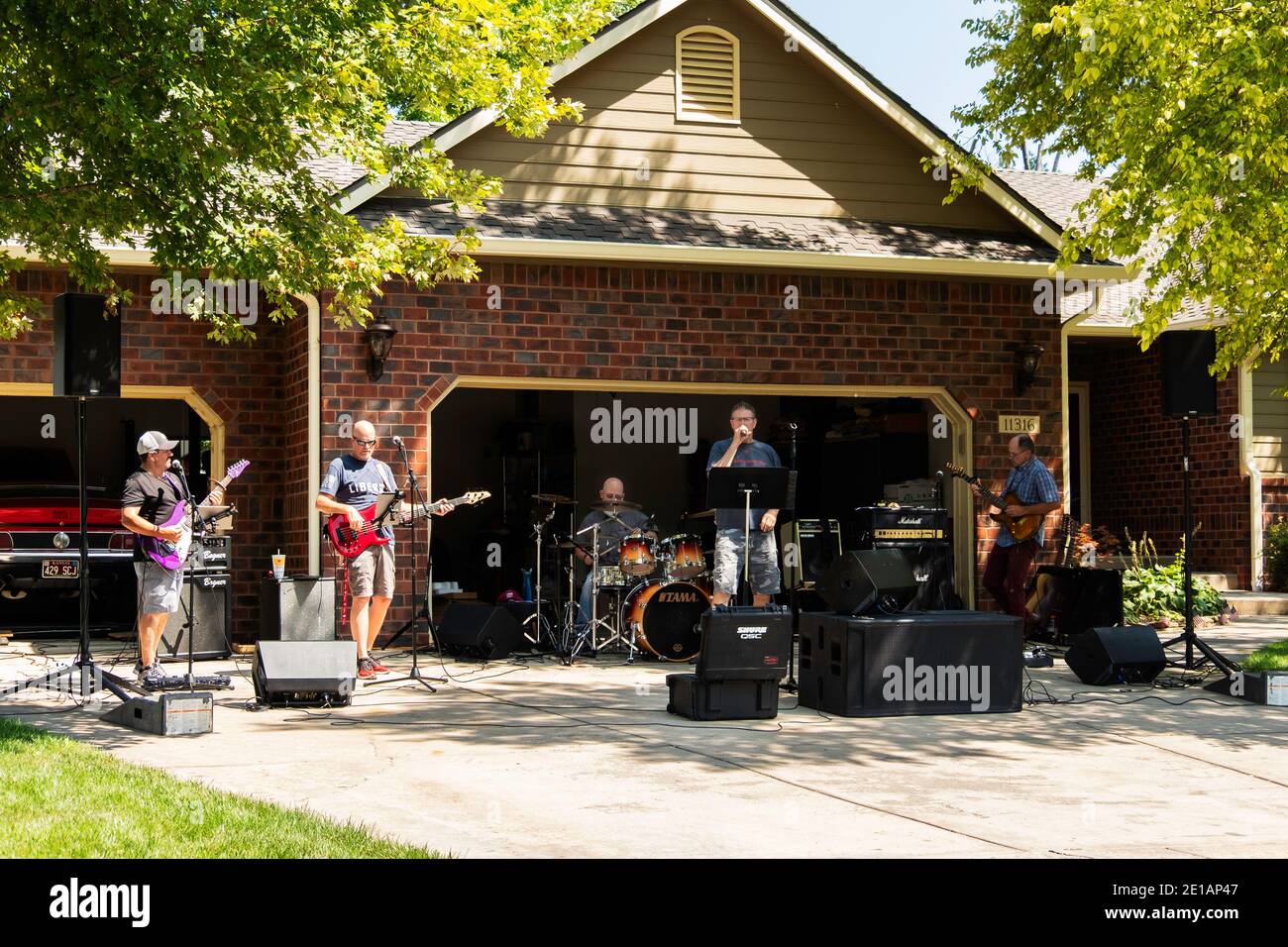 Erwachsene Männer in einer Garagenband üben für einen Gig oder ein Engagement, auf einer Auffahrt vor einer Garage im Sommer. Kansas, USA Stockfoto