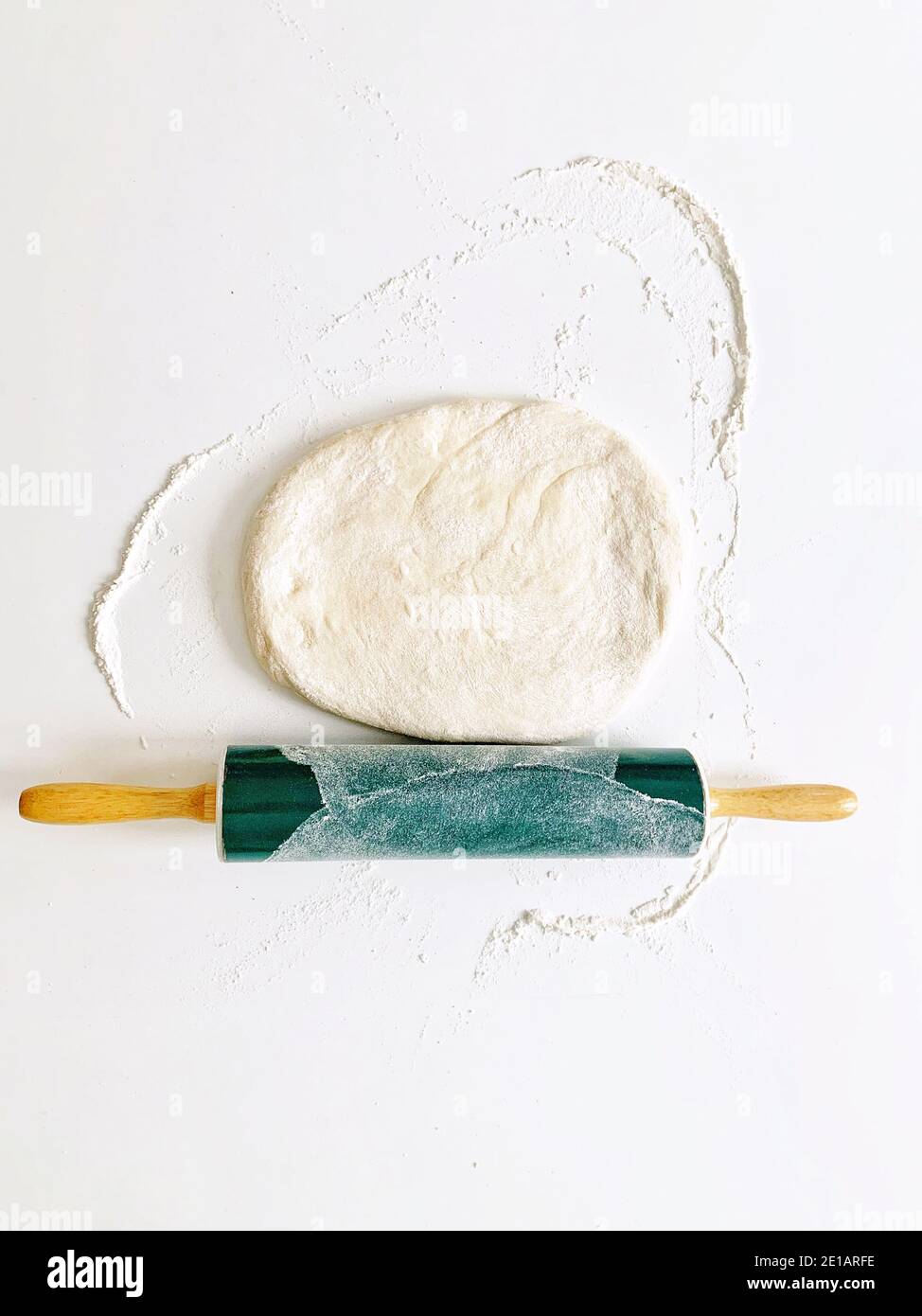 Weizenteig auf einem weißen Tisch und einem grünen Rollen PIN mit Mehl für die Herstellung von Brot und vorbereitet Pizza im Studio als Minimalismus-Konzept Stockfoto