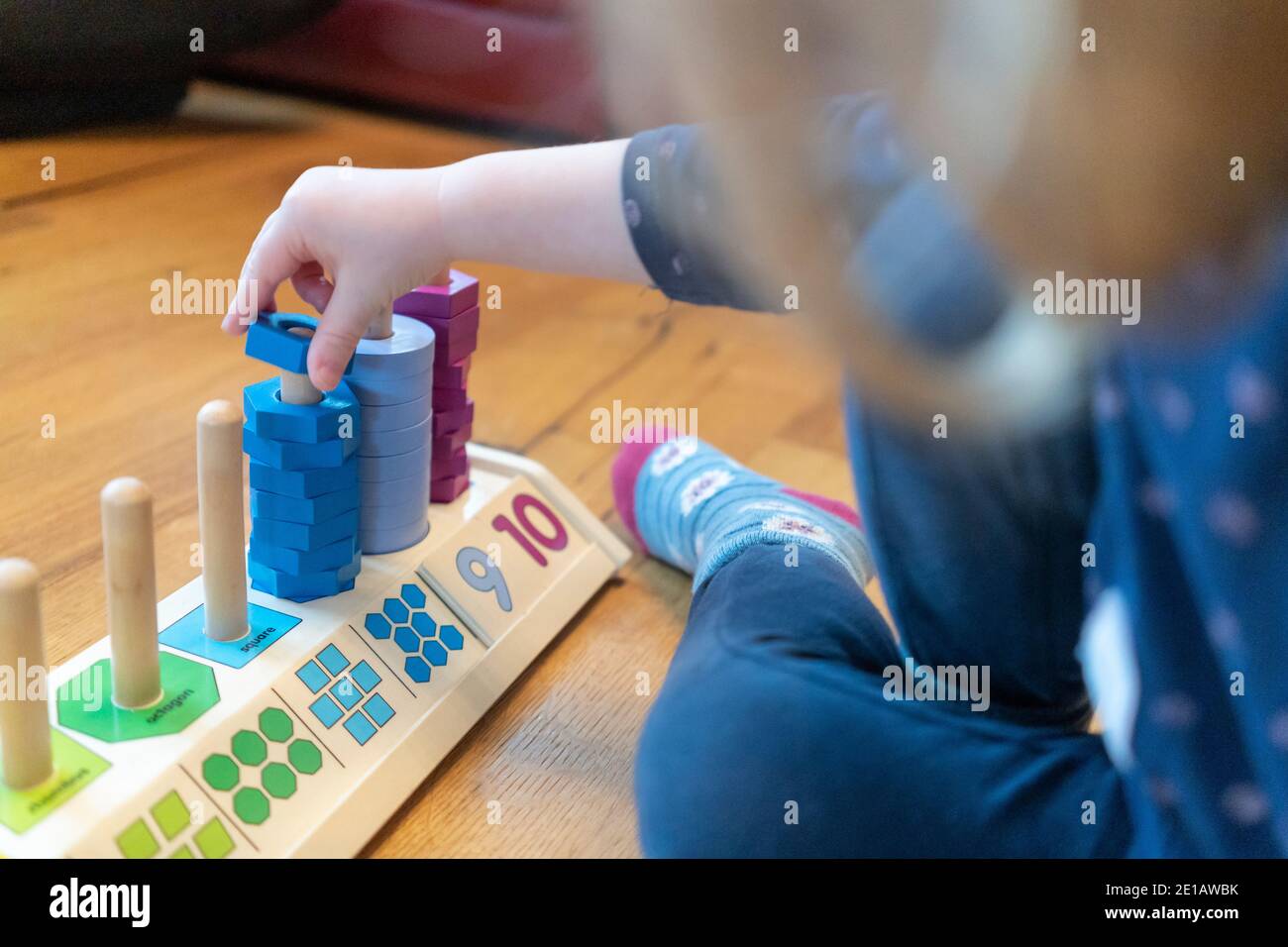 Ein junges, zweijähriges Kind sitzt auf dem Boden Und lernen, mit einem hölzernen Zählen Formen Stapler zählen Lernspielzeug Stockfoto