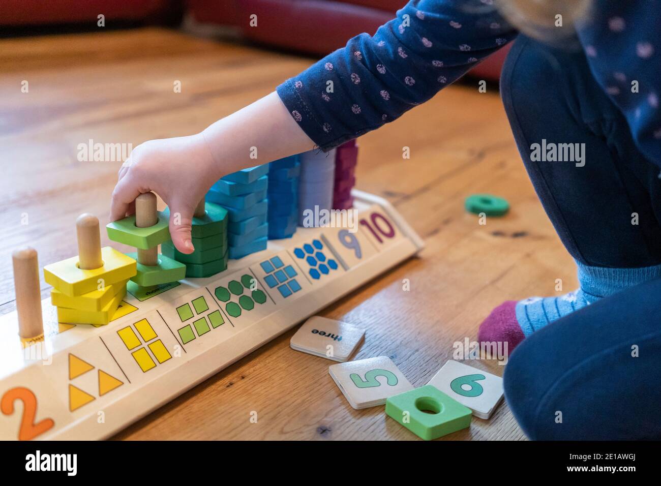 Ein junges, zweijähriges Kind sitzt auf dem Boden Und lernen, mit einem hölzernen Zählen Formen Stapler zählen Lernspielzeug Stockfoto