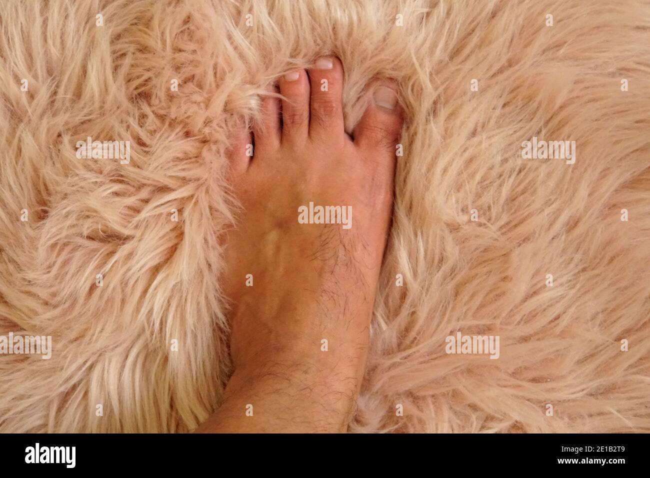 Ein Fuß steht auf einer weichen und pelzigen Pfirsichfarbe Decke Stockfoto
