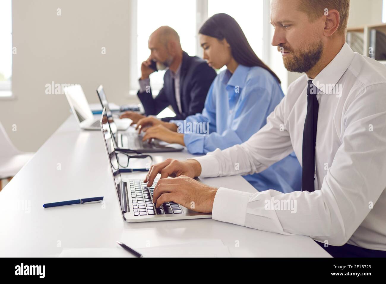Geschäftsleute, die im Büro zusammenarbeiten, sitzen in einer Reihe vor Laptops. Stockfoto