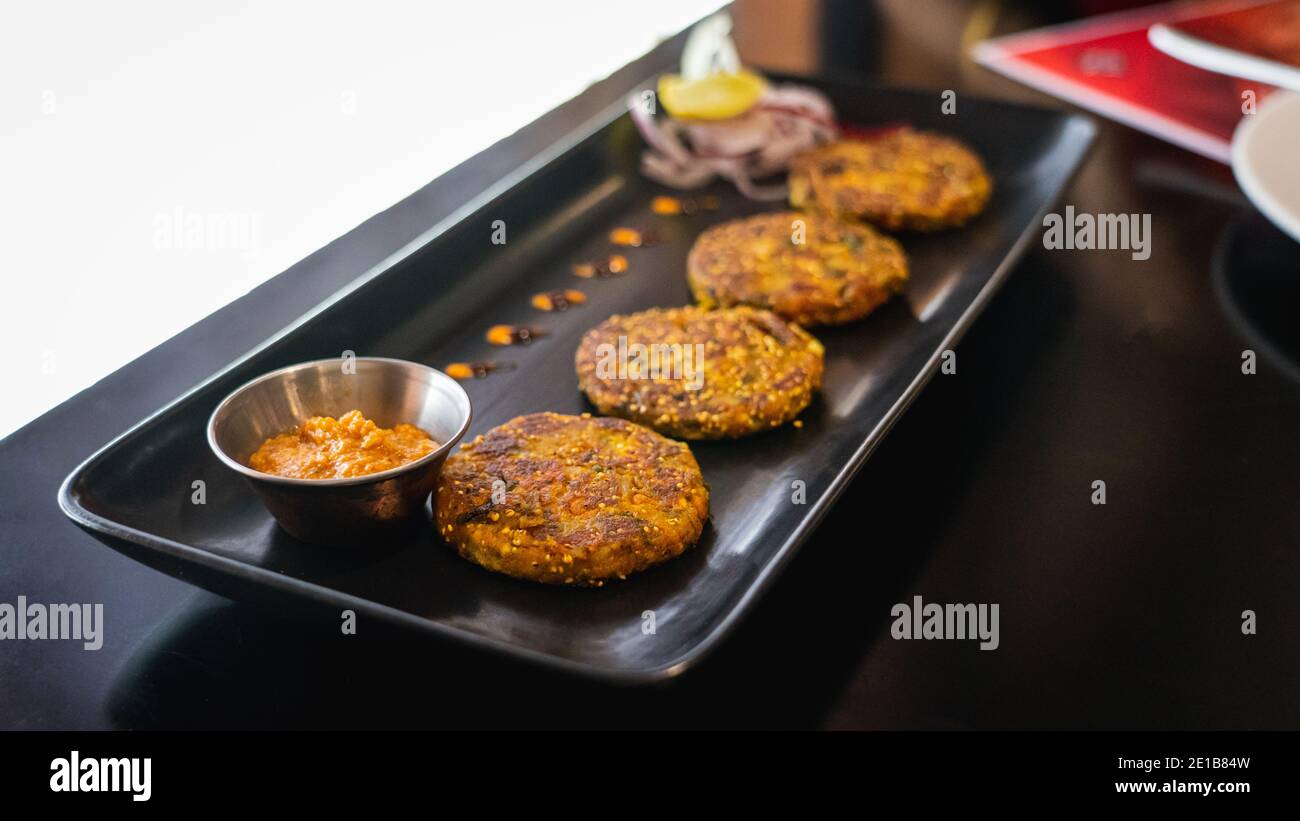 Selektive Konzentration von Quinoa-Patties mit rotem Pfeffer auf einem schwarzen Serviertablett serviert Stockfoto