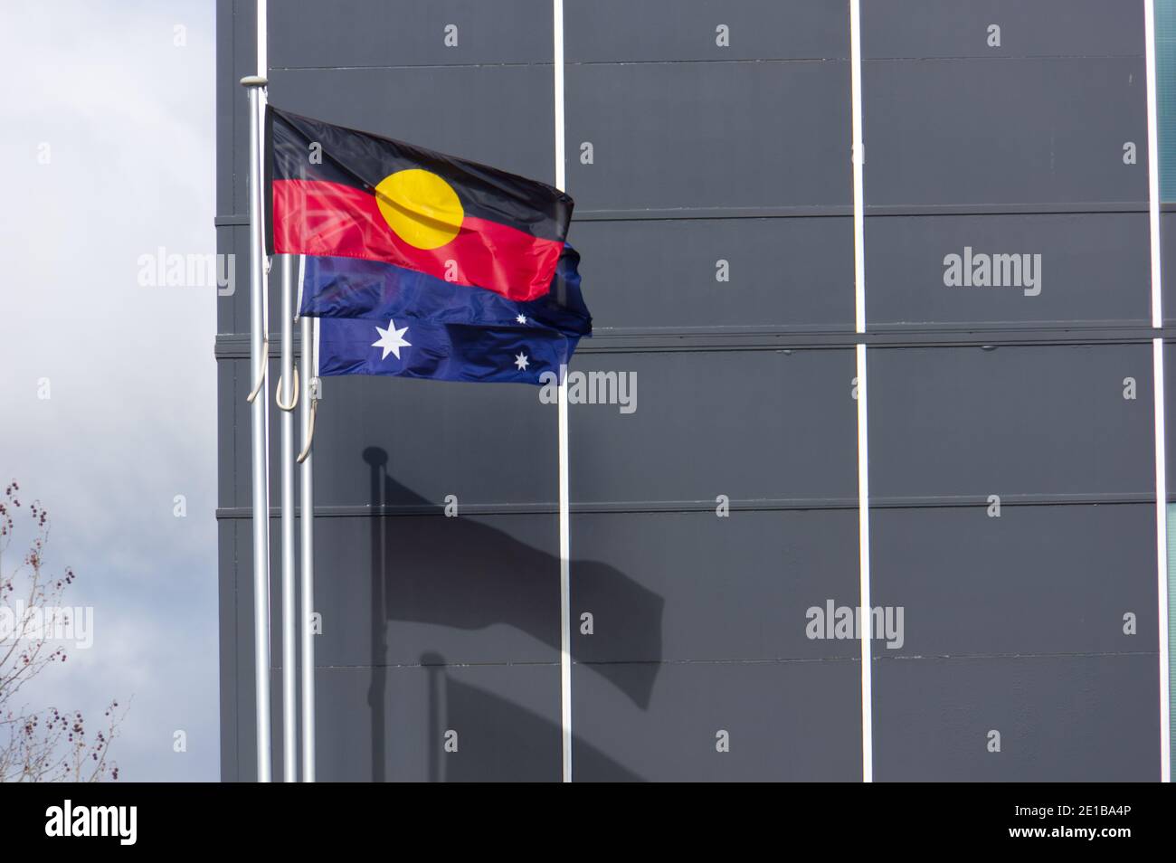 Einheimische Flagge und australische Flagge im Wind entfaltet neben einem Gebäude in Victoria, Australien. Stockfoto