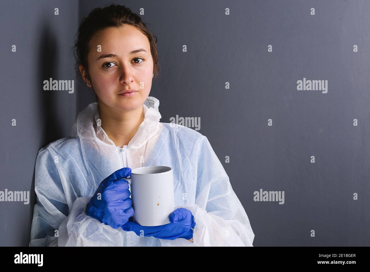 Junge Ärztin während einer Überarbeitungspause mit einer Tasse Kaffee an einer grauen Wand. Seitenraum. Stockfoto
