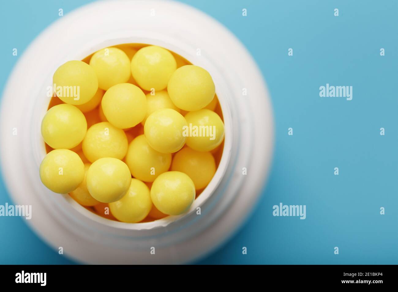Vitamine sind gelb in einem weißen Glas auf einem blau-blauen Hintergrund. Dragee Vitamin C. das Konzept der Gesundheit. Stockfoto