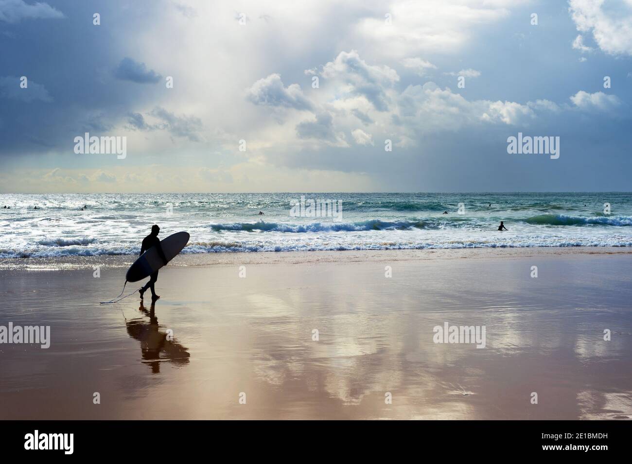 Surfer mit Surfbrett zu Fuß am Strand. Das Wetter war launisch. Algarve, Portugal Stockfoto