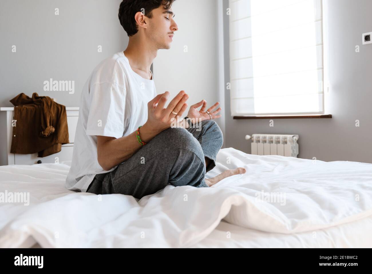 Bild eines konzentrierten Mannes, der zuhause auf dem Bett sitzt Und meditieren Stockfoto
