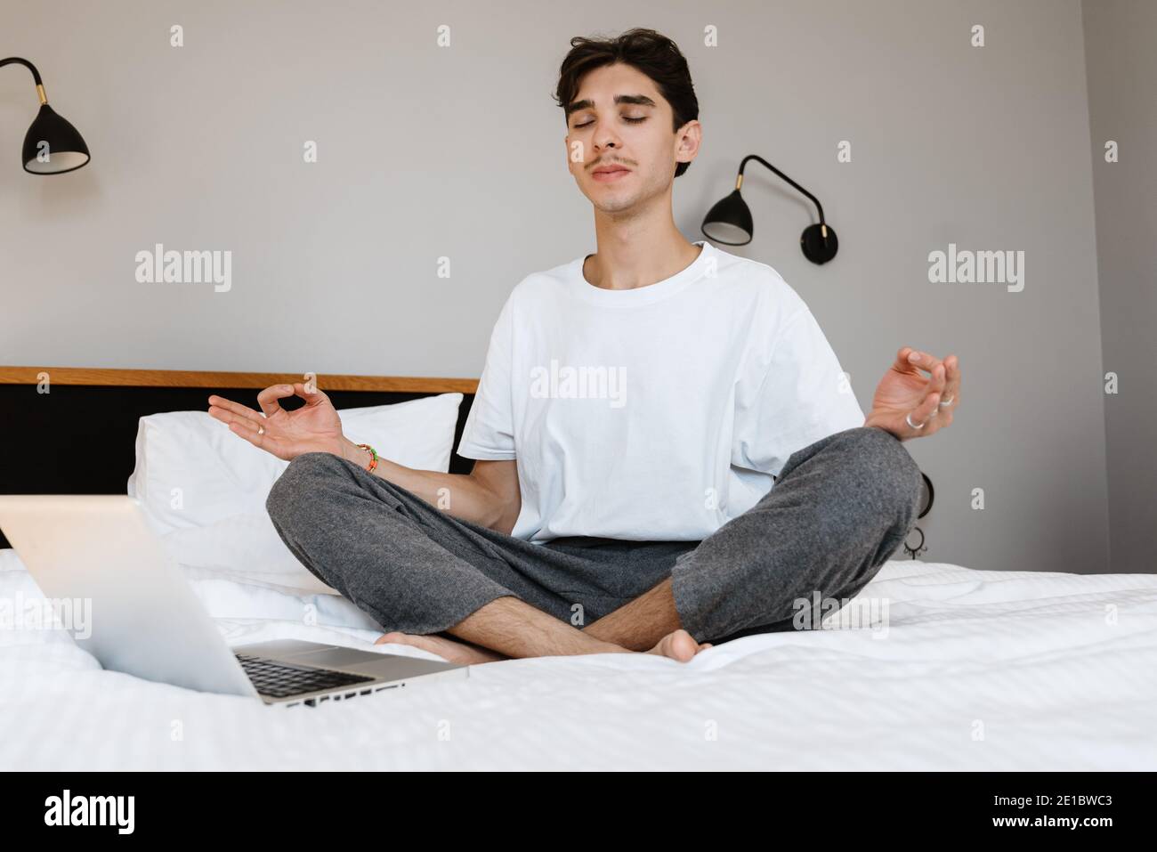 Bild eines konzentrierten Mannes, der zuhause auf dem Bett sitzt Und meditieren Stockfoto