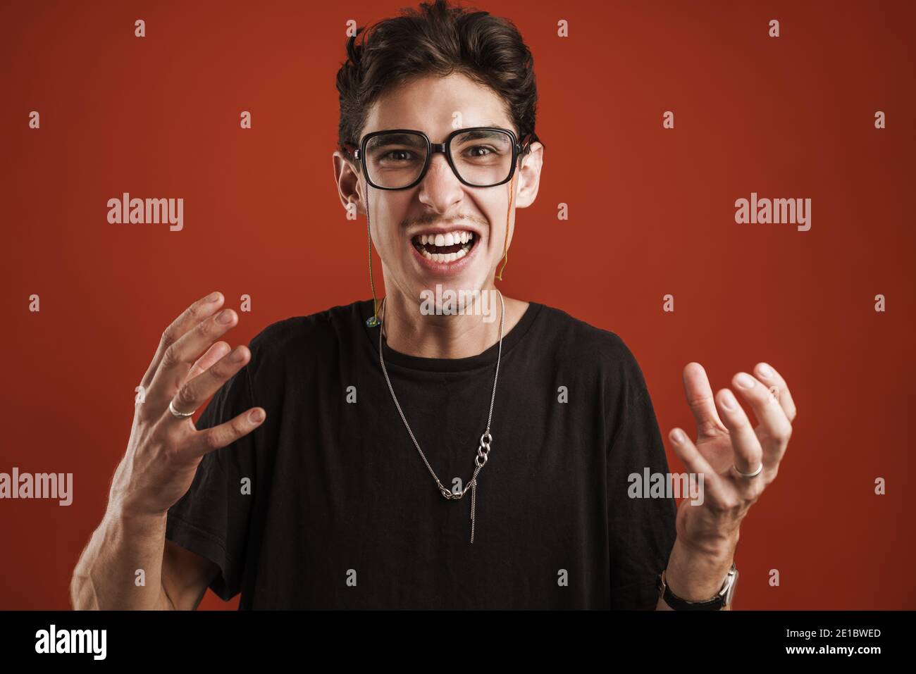 Wütend junge Hipster Kerl gestikulieren mit Händen isoliert über rot Hintergrund Stockfoto