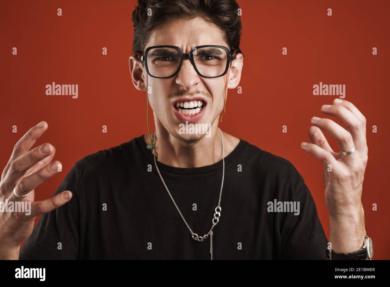 Wütend junge Hipster Kerl gestikulieren mit Händen isoliert über rot Hintergrund Stockfoto