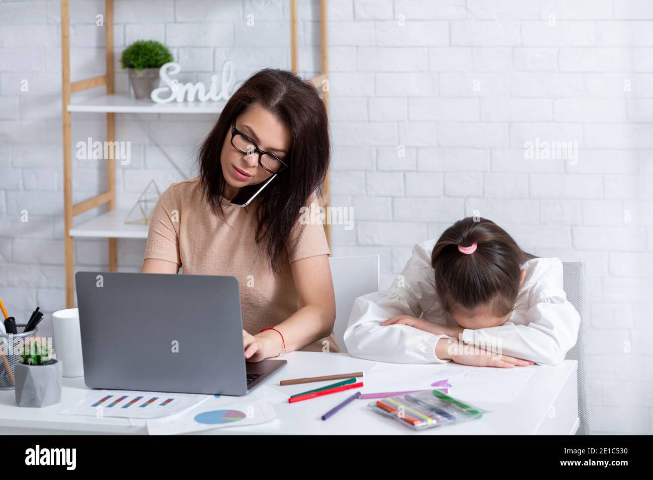 Beschäftigte Mutter, die am Laptop arbeitet und zu Hause telefoniert, einsames, depressive Kind, das in der Nähe sitzt Stockfoto