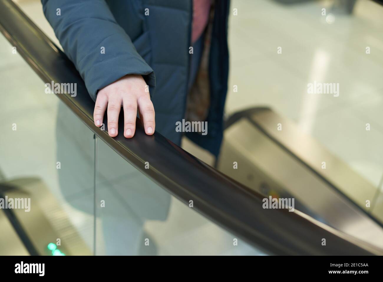 Weibliche Hand auf Rolltreppe Handlauf, Prävention und Virenschutz Konzept in Mall Stockfoto