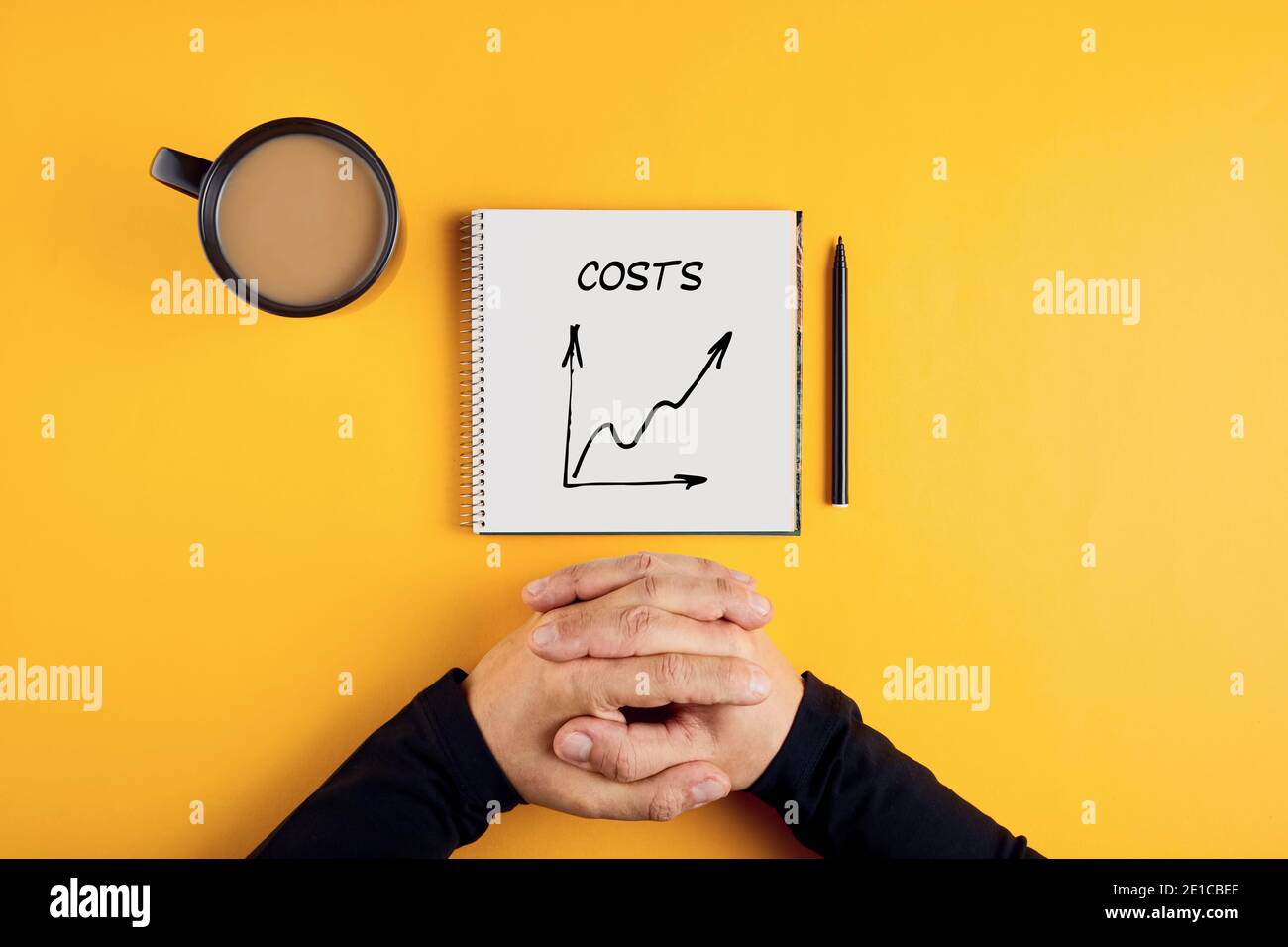 Hände eines Geschäftsmannes und ein Spiralnotizbuch mit dem Wort Kosten darauf geschrieben. Steigende oder steigende Geschäftskosten. Stockfoto
