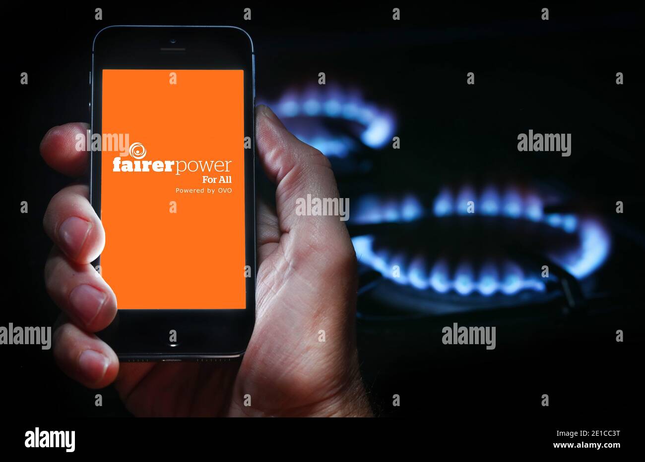 Ein Mann auf der Website Logo für Energieunternehmen gerechtere Macht auf sein Handy vor seinem Gaskocher (Editorial nur verwenden) Stockfoto