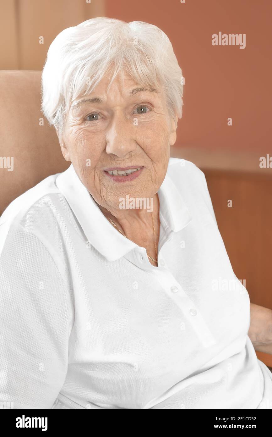 Fröhlich lächelnde ältere Frau in einem bequemen Stuhl in ihrem Zimmer in einem Altersheim. Stockfoto