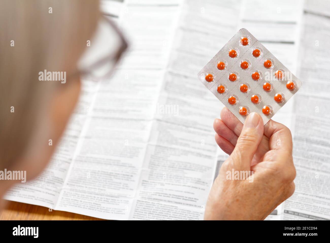 Ältere Frau hält ein Blatt oranger Pillen vor einer riesigen Drogenpackung. Gesundheitswesen und Medizin Konzept. Stockfoto