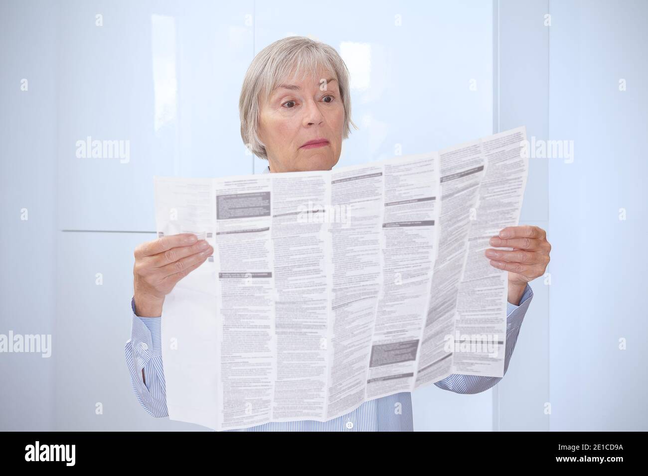 Betäubt ältere Frau mit einem riesigen Patienteninformationsblatt für ihre verordnete Medizin. Stockfoto