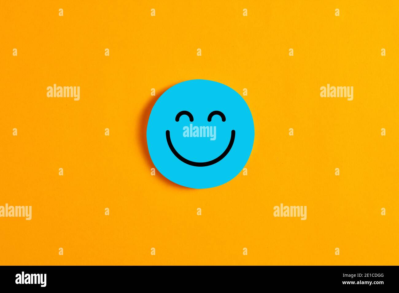 Blauer runder Kreis mit einem fröhlichen oder Smiley-Gesicht-Symbol auf ihm vor gelbem Hintergrund. Positiver Ausdruck oder Kundenzufriedenheit im Geschäftskonzept. Stockfoto
