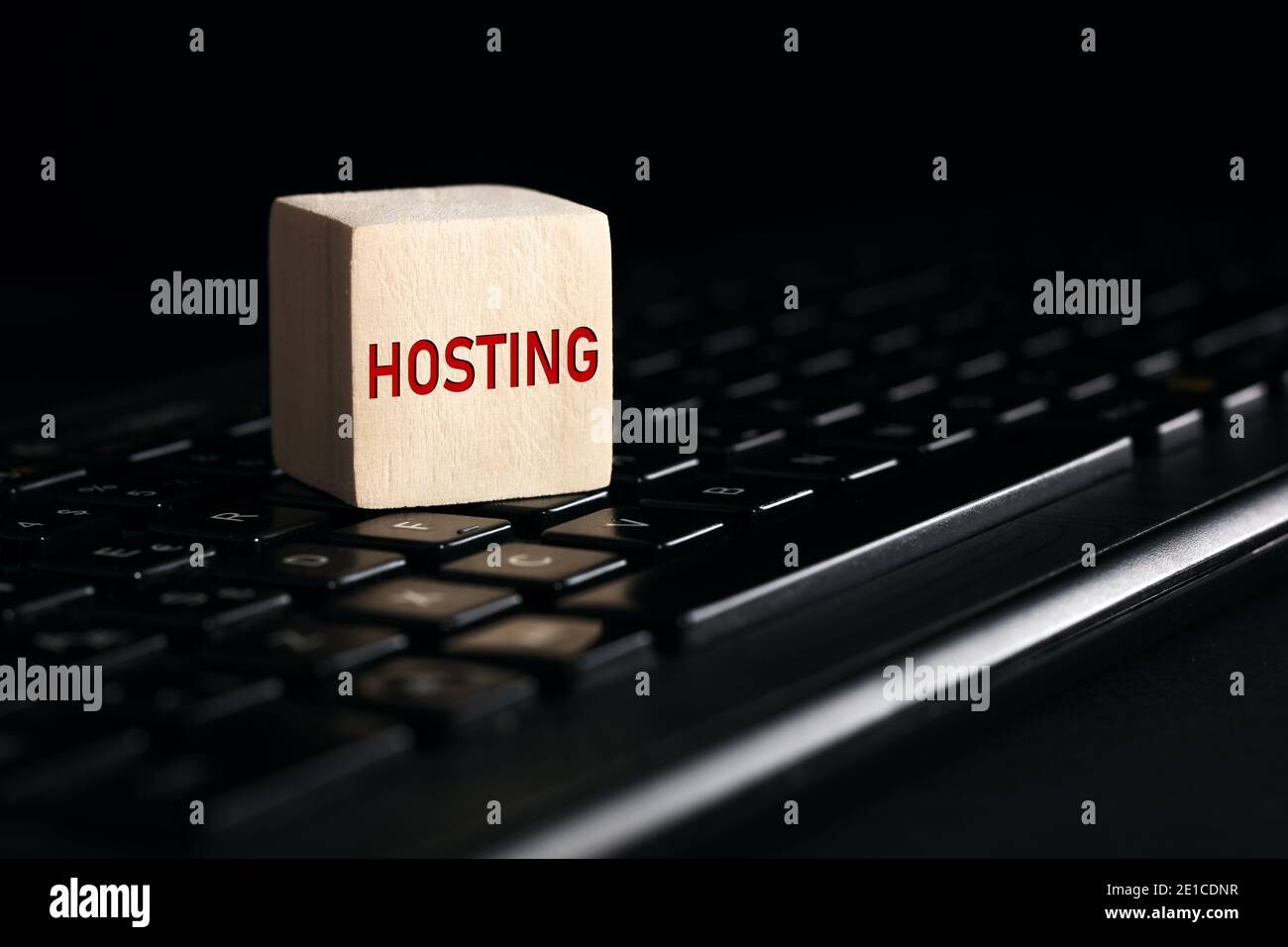 Das Wort Hosting auf Holzblock mit Computer-Tastatur vor schwarzem Hintergrund. Computer- oder Webhosting-Konzept. Stockfoto