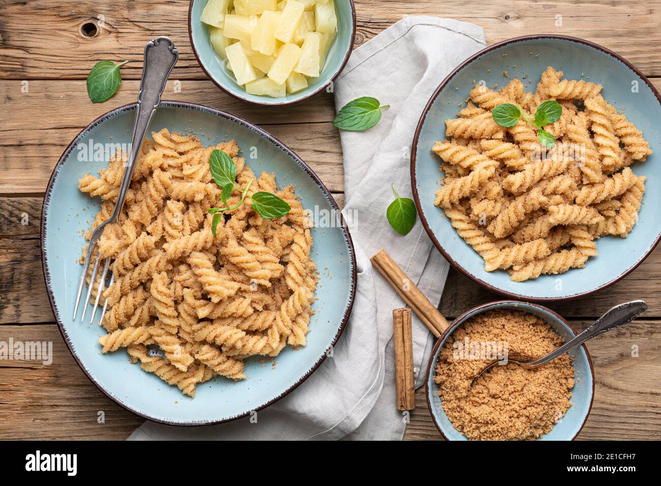 Einfache Fusilli-Pasta mit süß gebratenem Grieß und Zimt, serviert mit Ananasstücken Stockfoto