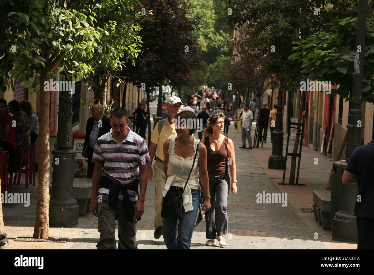 Fußgänger, die entlang einer von Bäumen gesäumten Straße spazieren. Calle de las Huertas in Madrid. Stockfoto