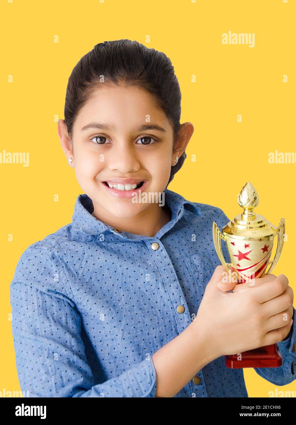 Portrait eines schönen und lächelnden indischen Schulmädchen in gelben Hintergrund mit einer goldenen Trophäe und Darstellung Sieg. Stockfoto