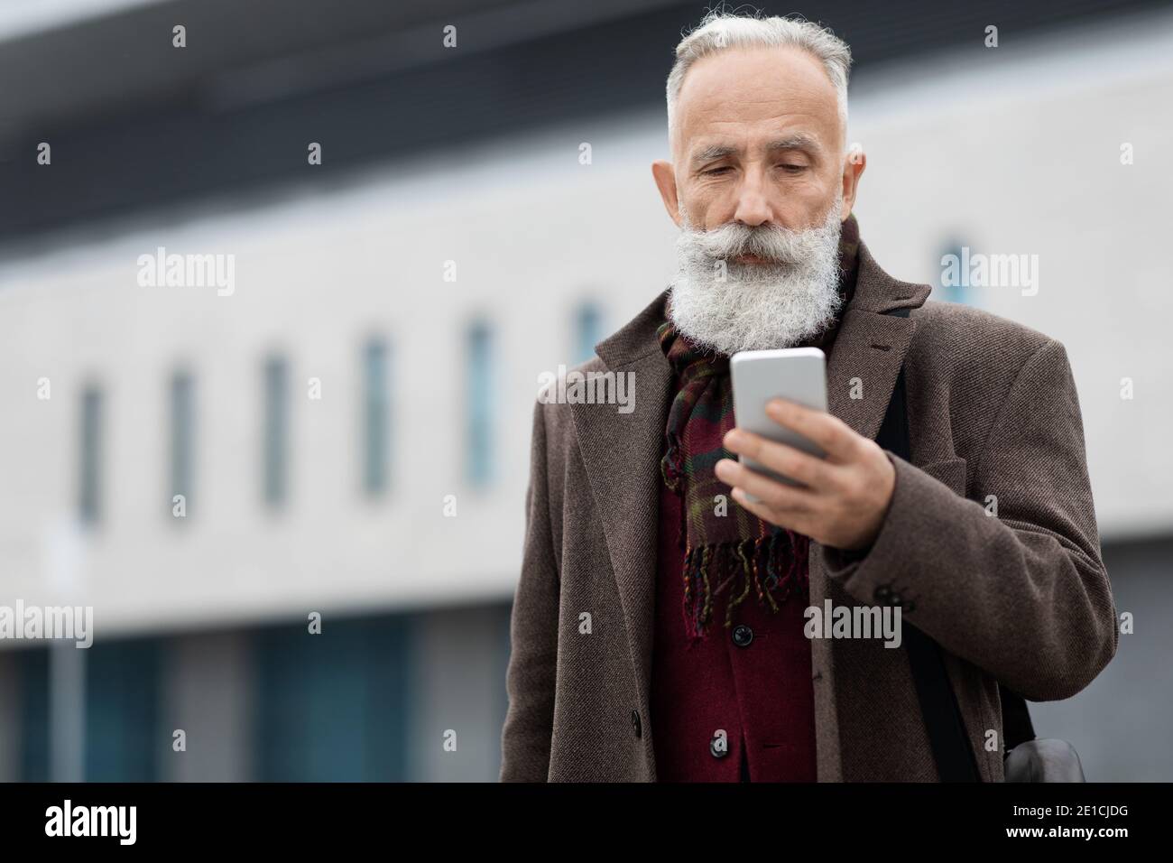 Wohlhabender älterer Mann überprüft sein modernes Smartphone Stockfoto