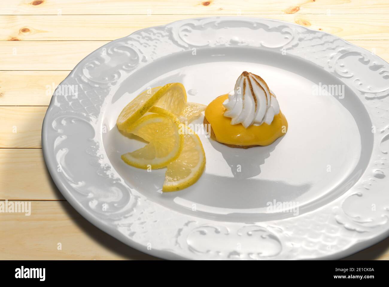 Zitronencreme-Tarte mit Baiser Brule und Zitronenscheiben Weißer Teller auf Holztisch Stockfoto