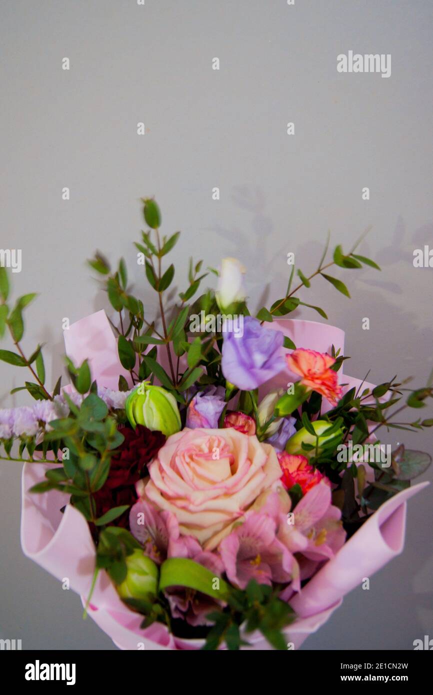 Zartes Bouquet von verschiedenen Blumen in einem hellrosa Wrapper auf grauem Hintergrund. Vertikales Foto. Stockfoto