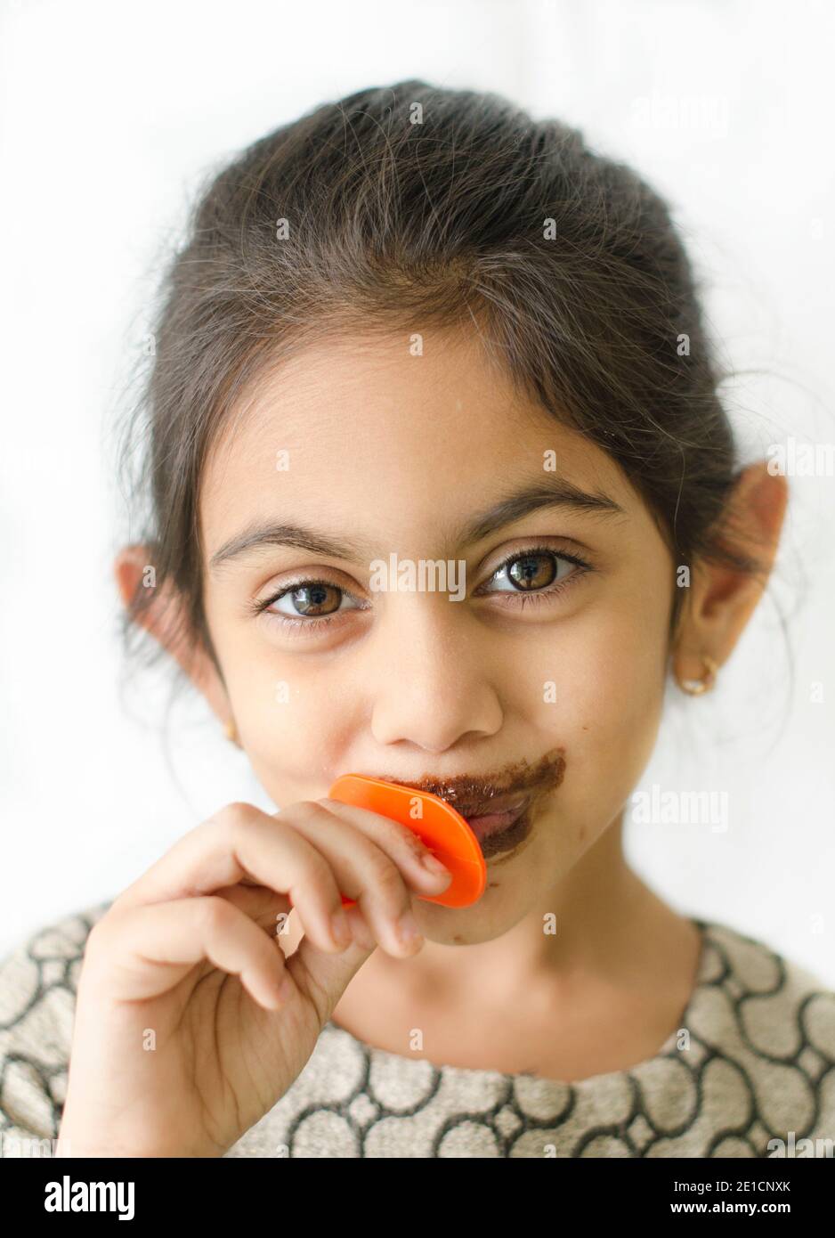 Lächelnd kleine indische Mädchen Kind genießen essen Eis Stick mit Flecken um ihren Mund. Stockfoto
