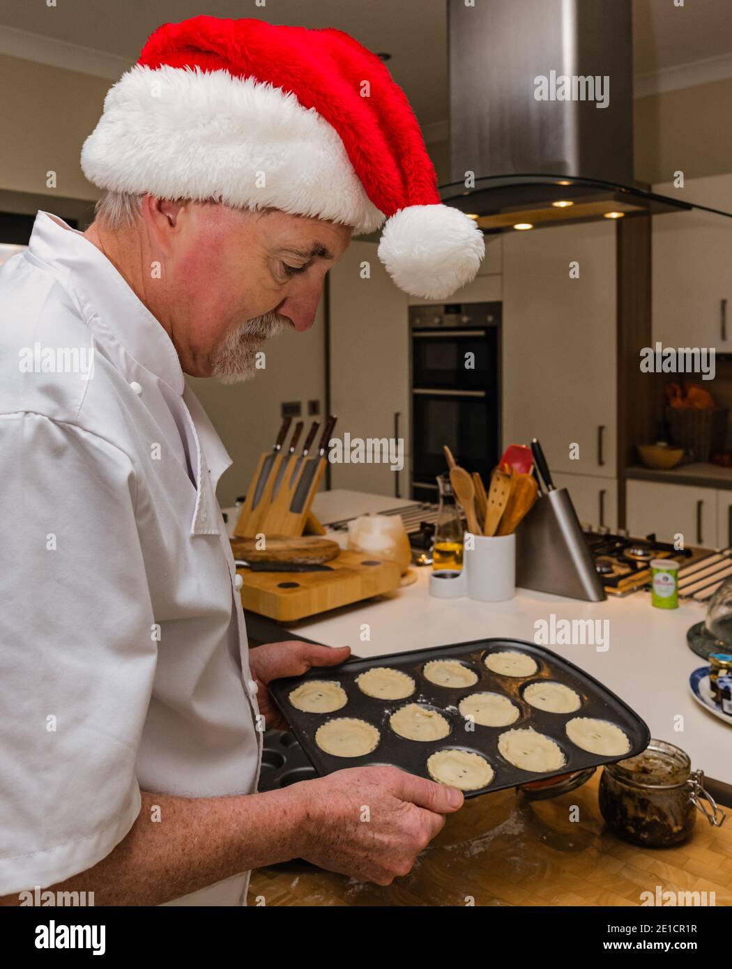 Senior Mann trägt Koch weiß und Santa Hut Herstellung von Hackfleisch Torten zur Weihnachtszeit in einer heimischen Küche Stockfoto
