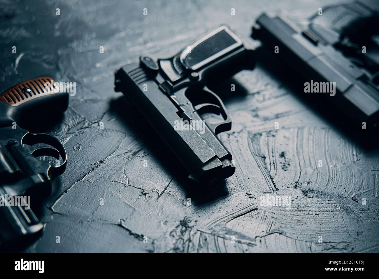 Gruppe von Pistolen auf schwarzem Betontisch. Vintage Revolver mit einer Trommel. 9-mm-Pistole. Mehrere Arten von gefährlichen Schusswaffen. Kriminelles oder polizeiliches Arsenal. Stockfoto