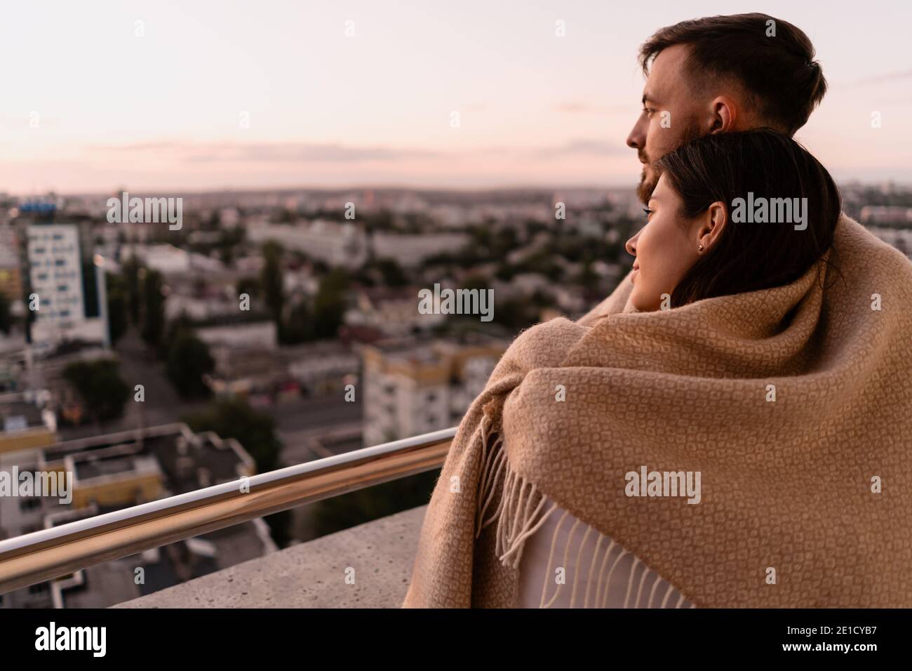 Nahaufnahme Porträt, Mann und Frau lächeln einander bei Sonnenuntergang mit Stadt im Hintergrund. Romantische Momente im intimen Kreis Stockfoto