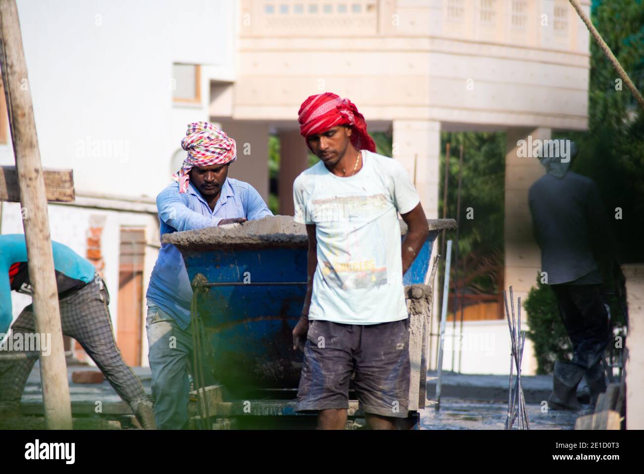 Zoomed in Schuss von indischen unterprivilegierten Bauarbeiter mit Sand, Zement, Steine und Wasser auf dem Kopf, um in einen Mixer zu laden, um zu machen Stockfoto