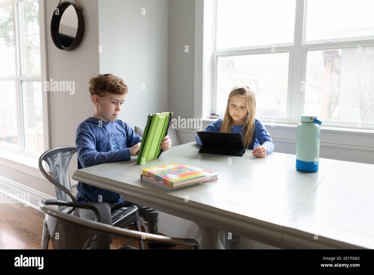 Kinder Geschwister arbeiten an Tablets zusammen drinnen am Küchentisch Stockfoto
