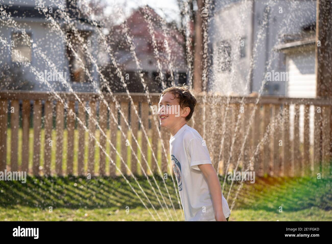 Junge spielt im Wasserregner im Hinterhof Stockfoto
