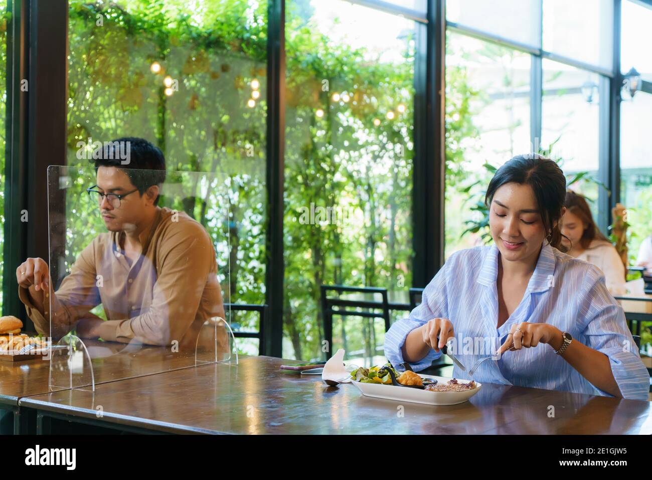 Asiatische Frau und Asiaten Essen allein am Tisch mit Plexi Bildschirm zwischen Tisch in Wiedereröffnung Restaurant nach Lockdown Maßnahme. Stockfoto